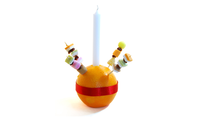 Orange with sweets and a candle stuck in and a red ribbon around it.